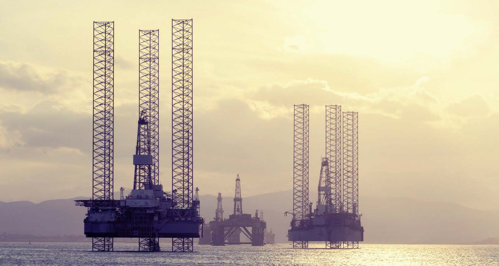 Offshore oil drilling platforms stand in a tranquil sea with soft golden sunlight