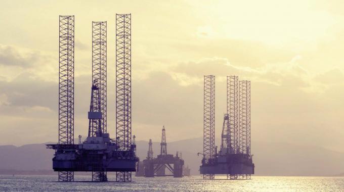 Offshore oil drilling platforms stand in a tranquil sea with soft golden sunlight